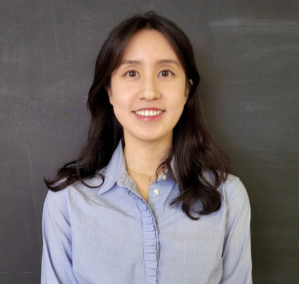 A person with black hair and brown eyes wearing a blue button-down shirt.